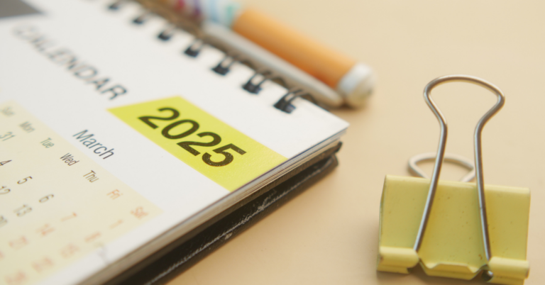 Close up of a desk with 2025 calendar with March shown, pen and yellow binder clip