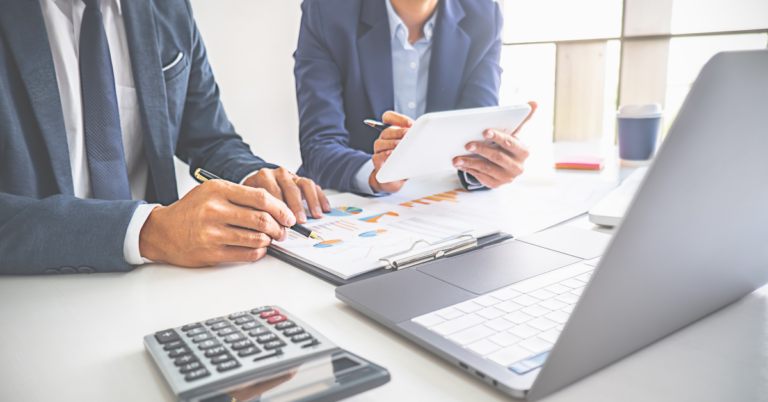 close up of a professional man and woman reviewing financial documents at a desk with a laptop, tablet, calculator and papers