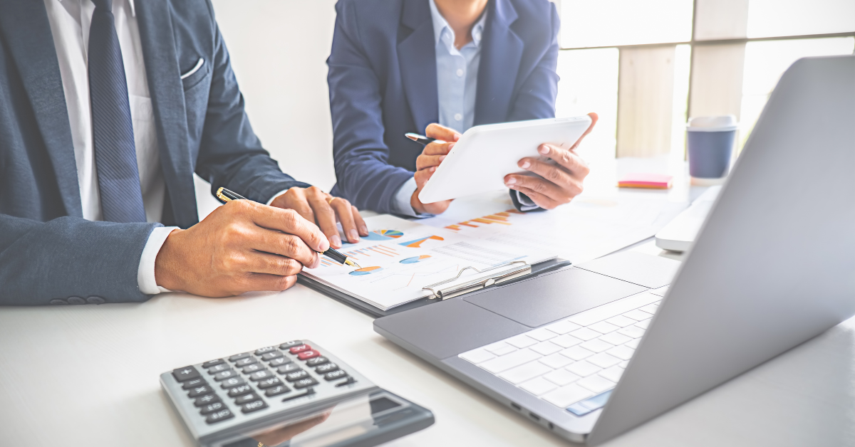 close up of a professional man and woman reviewing financial documents at a desk with a laptop, tablet, calculator and papers